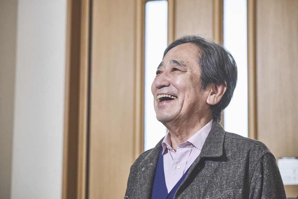 髙橋豊を演じるルー大柴。明るい窓辺で顔をほころばせて笑う。