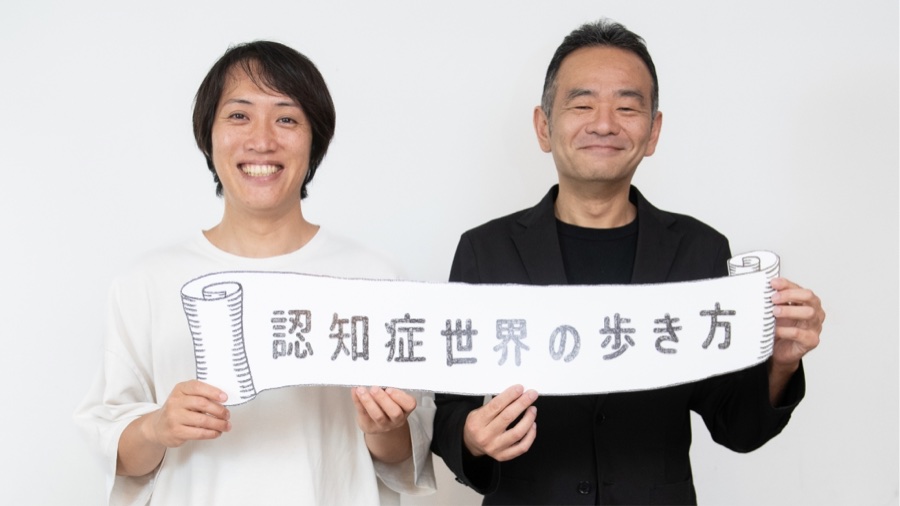 『認知症世界の歩き方』と書かれた横断幕を持つ2人