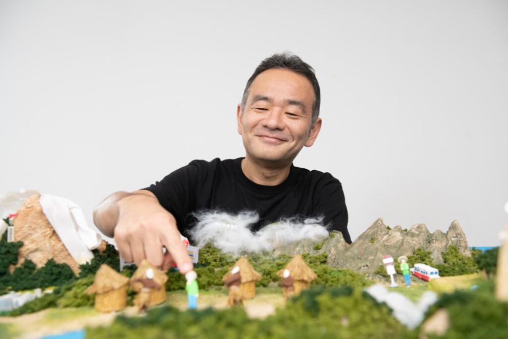 『認知症世界の歩き方』の世界を再現したジオラマに人形を置く、原作者の筧裕介。